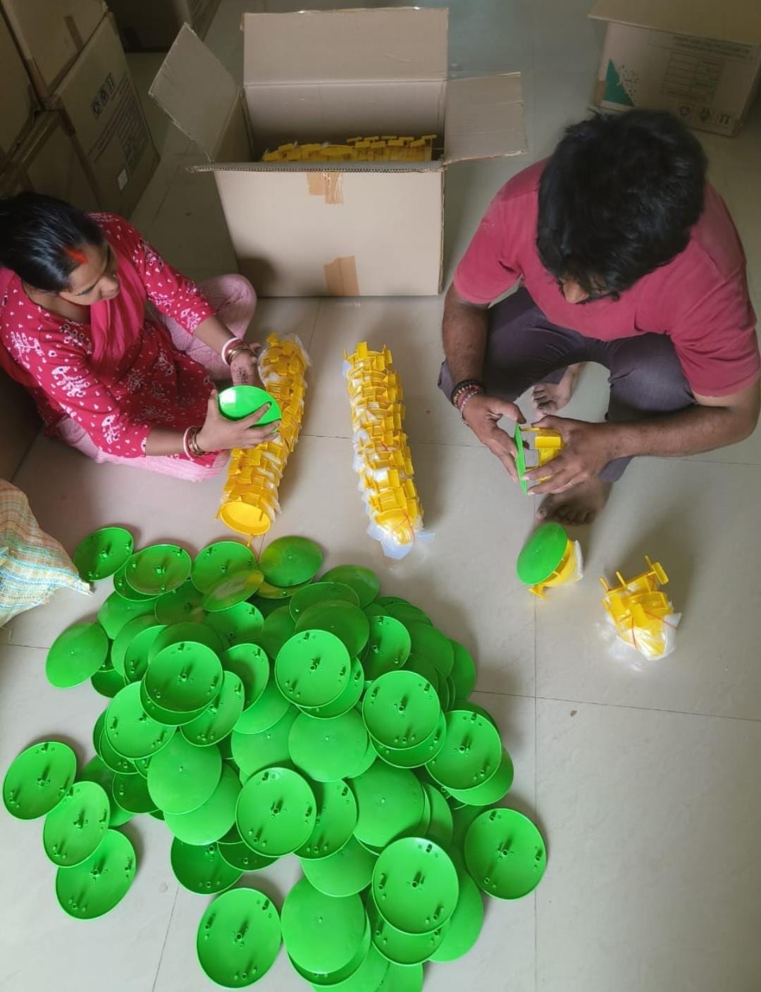 Workers assembling funnel pheromone traps from green lids and yellow funnel parts on a warehouse floor in Hyderabad
